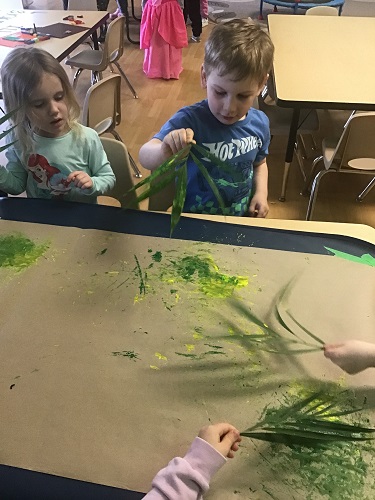 Preschool children painting with palm leaves