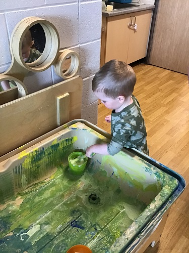 A child cleaning the paint off the inside of a sensory bin