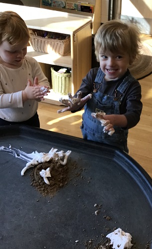 Two children standing at a tuff tray playing with sand and shaving cream