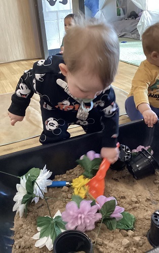 An infant scooping up some sand from the sensory bin