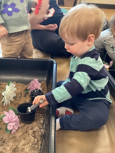 An infant sitting in front of a sensory bin filled with sand and flowers