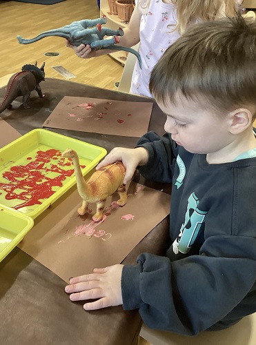 A child using a toy dinosaur to create foot prints in paint