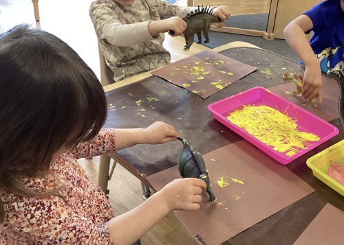 children using dinosaurs to make footprints on paper