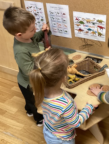 Children comparing toy dinosaurs to the posters on the wall