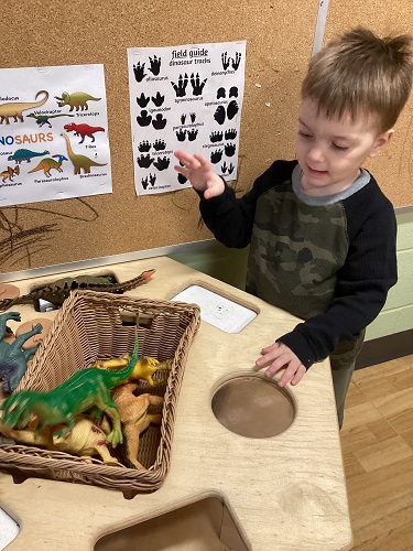 A child standing at a table with dinosaurs and posters beside him