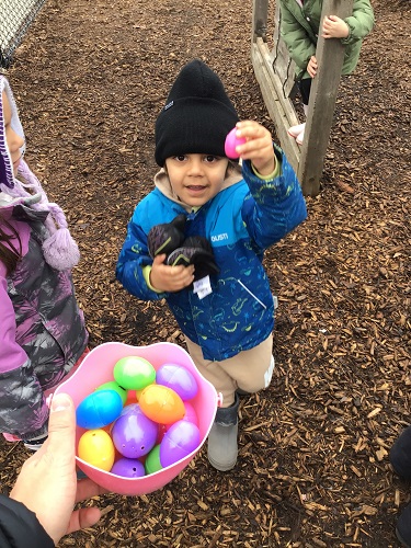 A child showing off the egg he is putting into the basket