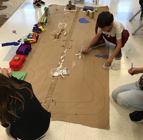 Children drawing roads on a large paper city they've created
