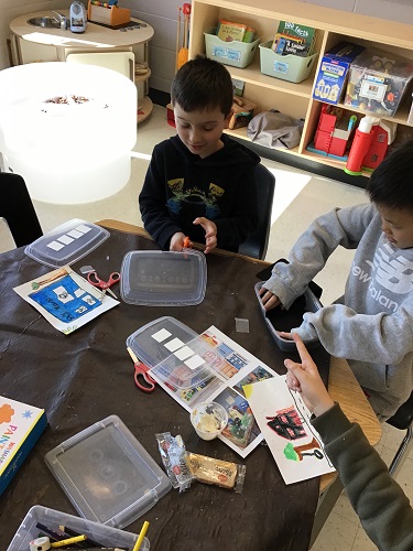 Children at a table using recycled materials to create buildings