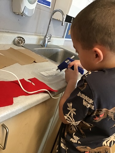 A child standing at a counter using a glue gun