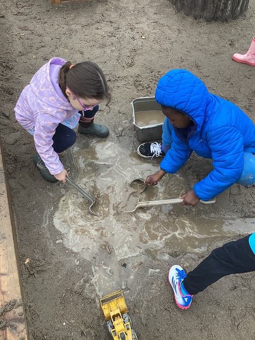 2 school age children scooping mud