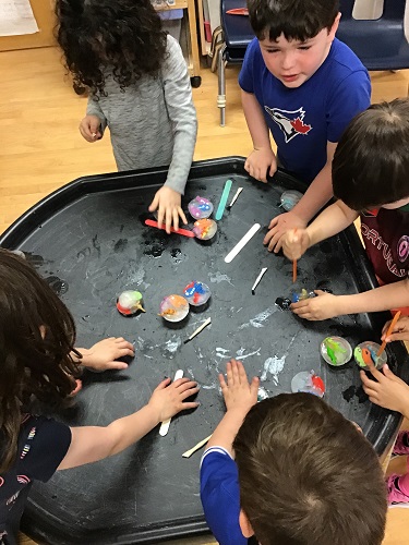 A group of school aged children using their hands to melt small ice pucks with plastic animals frozen inside