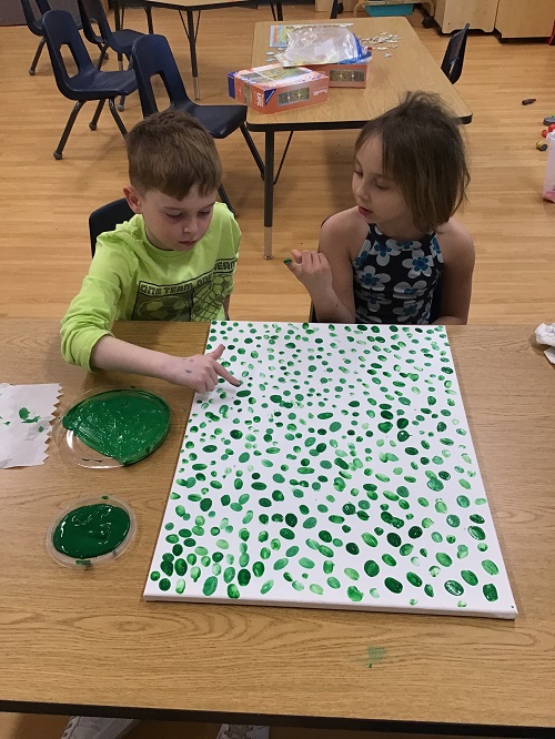 2 school age children painting on a canvas