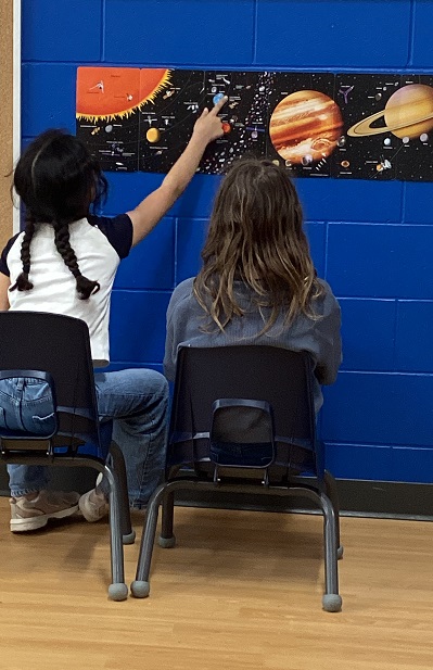 2 school age children looking at a map of the solar system