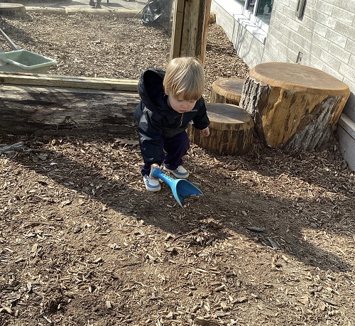 An infant child scooping up woodchips