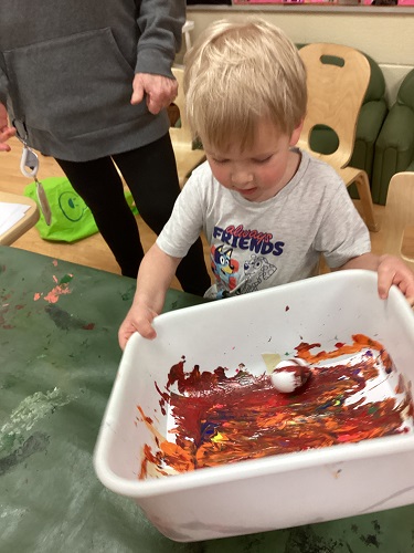 A preschool child rolling a plastic egg in paint to decorate it