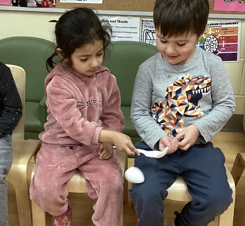 Two preschool children passing an easter egg from one spoon to the other spoon