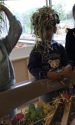 When looking for easter eggs in shredded paper a preschool child explores putting the paper on their head