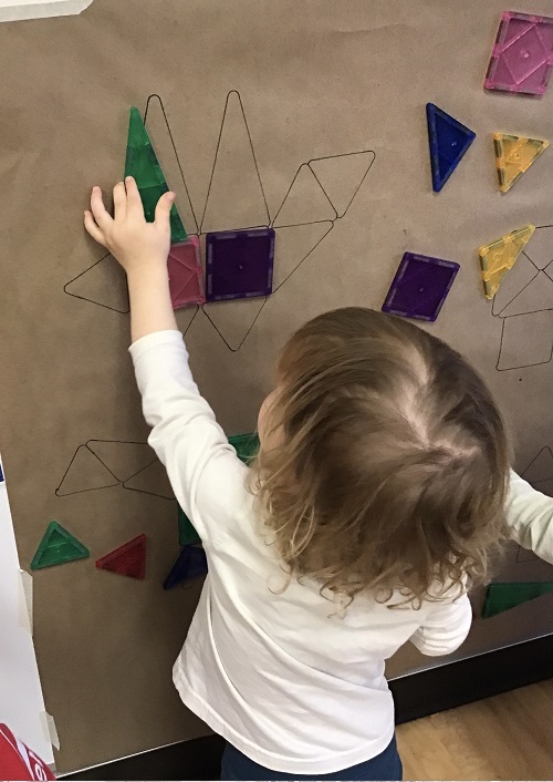 child exploring magnatiles on a dinosaur outline