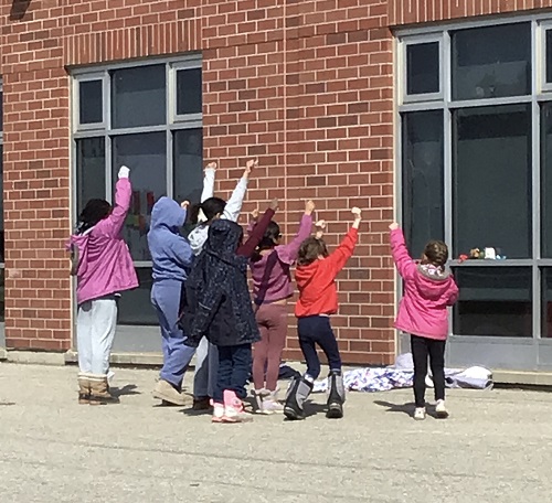 a group of children standing in front of a brick building with their hands in the air