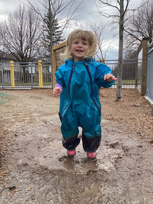 child smiling while standing in a puddle