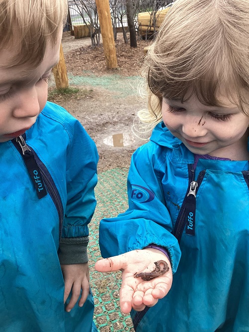child examining a worm in another child's hand