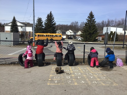Children sitting on the tires, looking at the school bus.