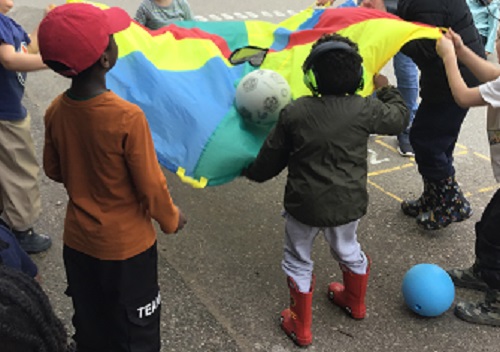 Group of children waving the parachute together.