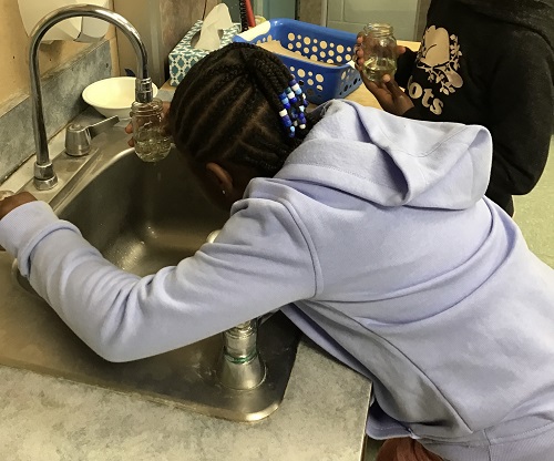 Child filling her glass bottle with water.