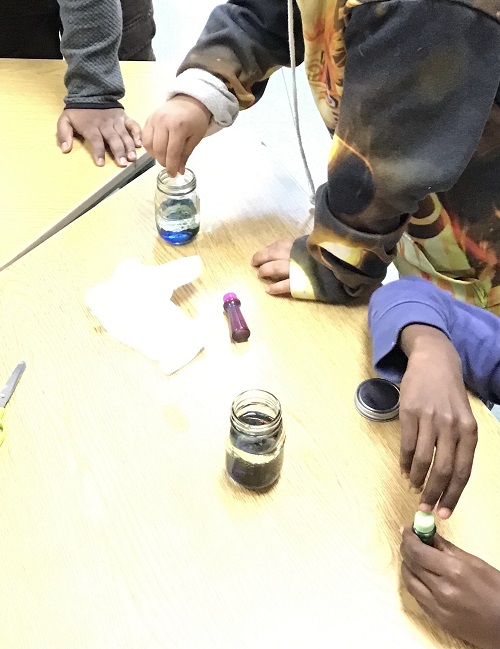Children putting food colouring in their glass bottles.