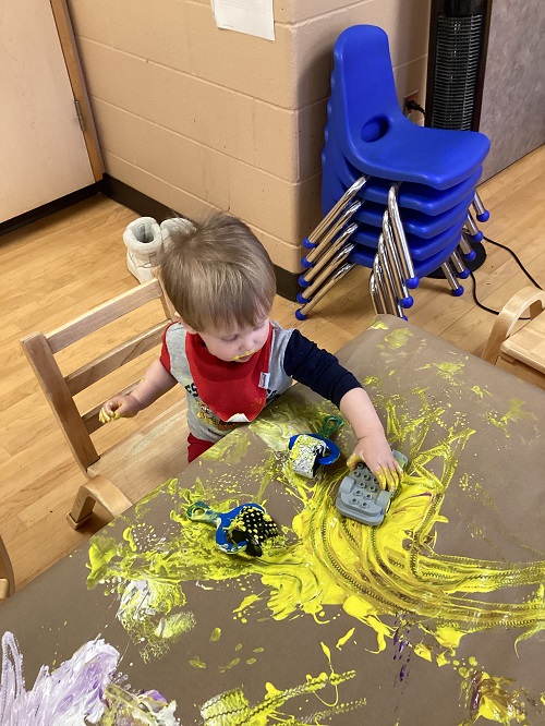 Child painting with cars on brown paper.