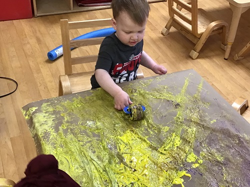 Child using a paint roller over the yellow paint.