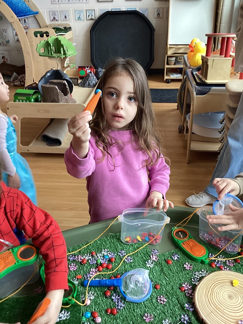 A preschooler child holding a pom pom with tweezers