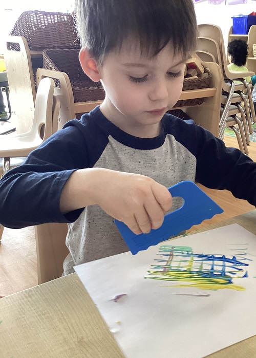 A preschool child using a scraper tool on their art works