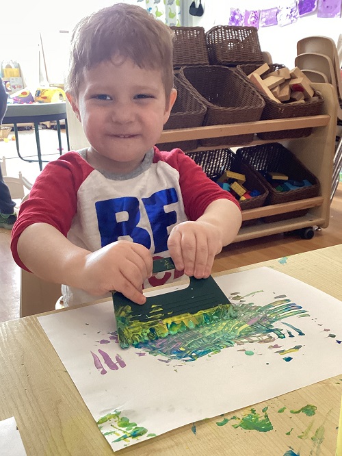 A preschool child using a scraper tool on their art work