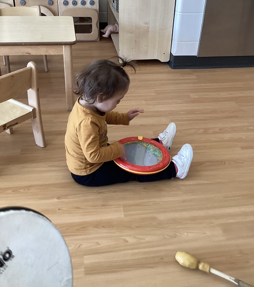 A toddler child exploring a drum with colourful beads inside