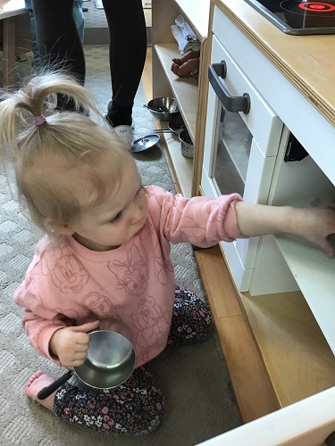 An infant putting dishes in the pretend kitchen