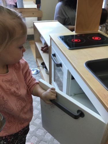 An infant opening the door to the pretend kitchen