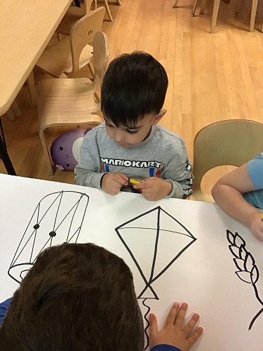 A group of children looking at drawings of a drum, kite and grains after discussing the Vaisakhi celebration with their educators