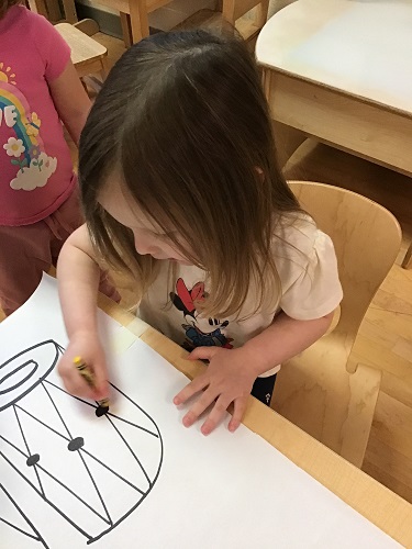 A preschool child colouring a picture of a drum