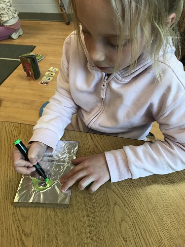 A school aged child using markers to colour the foil Easter egg they created