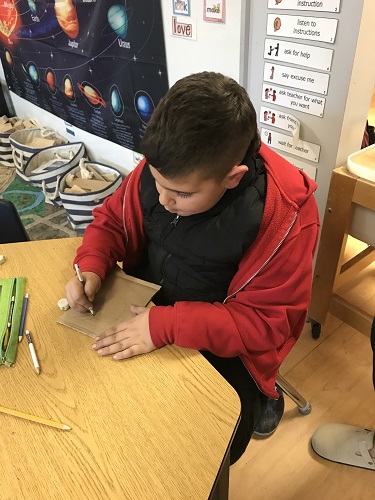 A school aged child drawing on a piece of cardboard