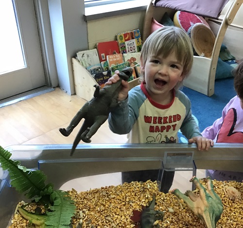 A toddler holding up a plastic dinosaur while roaring