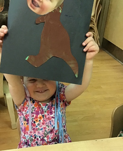 A toddler holding up their dinosaur picture